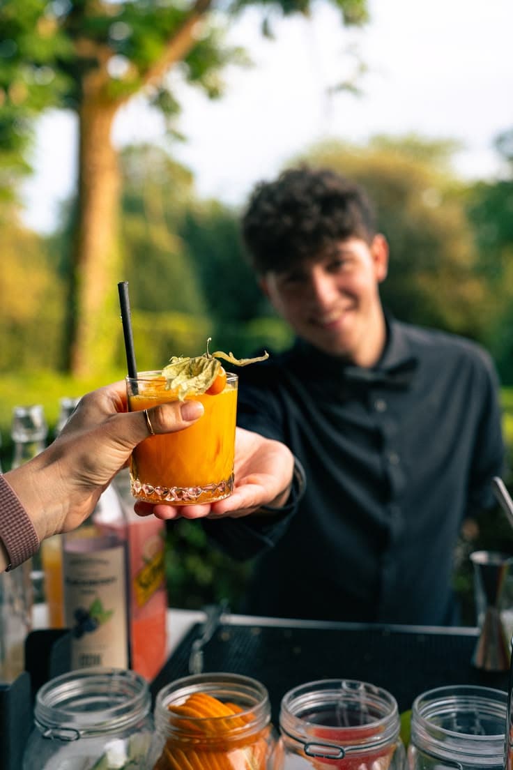 Bartender entrega un cóctel frente a una barra al aire libre