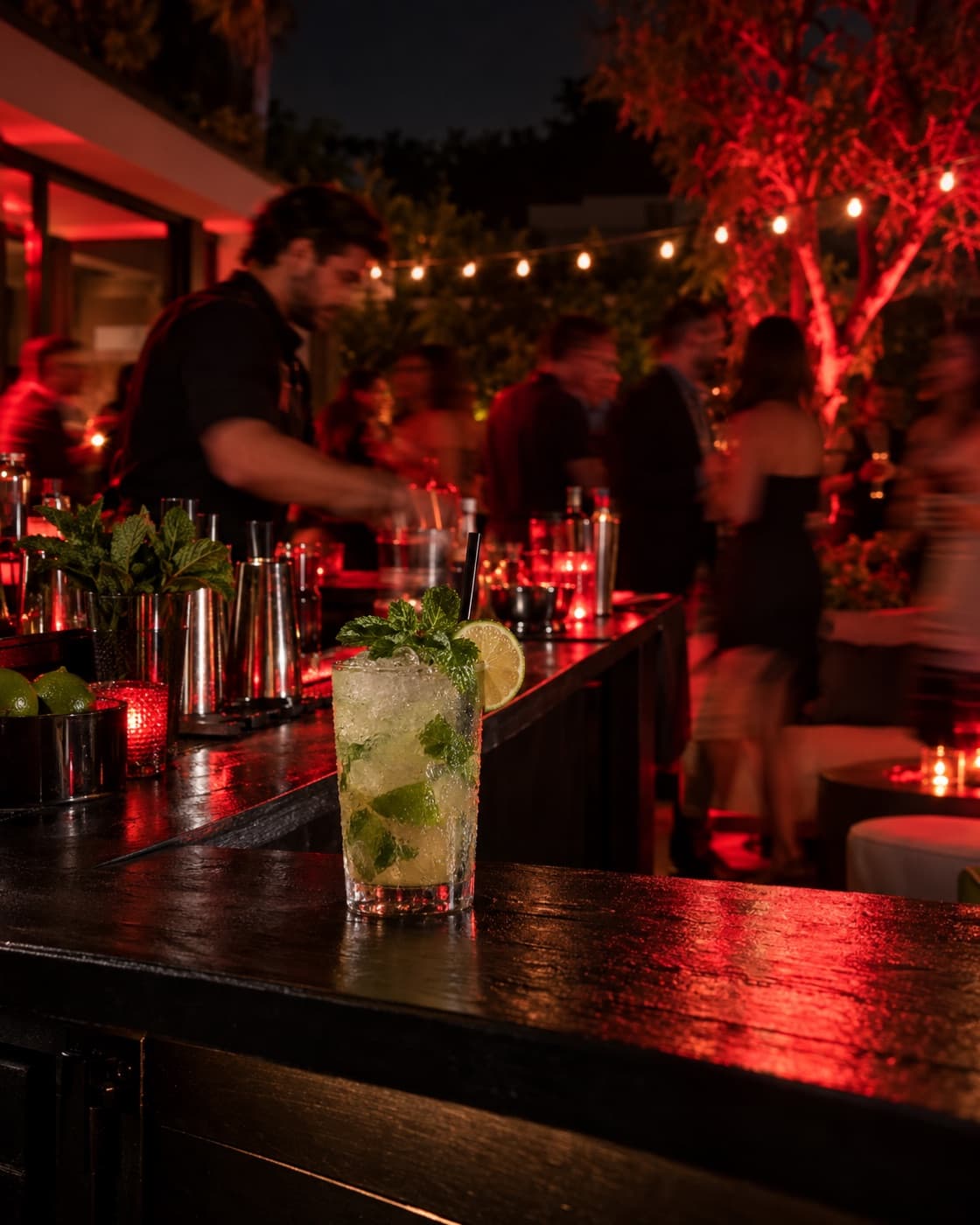 Mojito sobre una barra móvil negra en un cumpleaños de patio con invitados y luces rojas