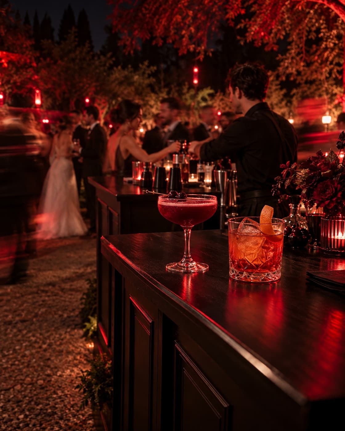 Cócteles sobre una barra móvil negra en un matrimonio al aire libre con luces rojas